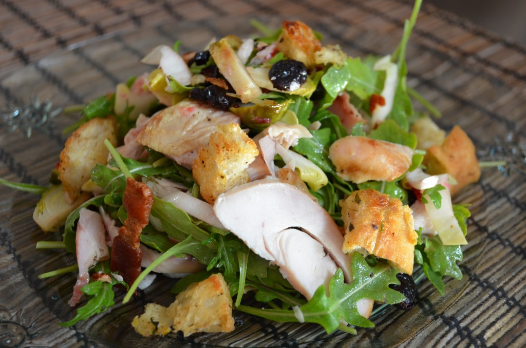 a plate of salad with sliced turkey, croutons, bacon, cranberries showing