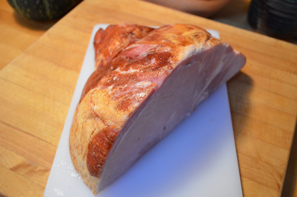 a cut piece of bone-in ham sitting on a white cutting board, on a wooden counter