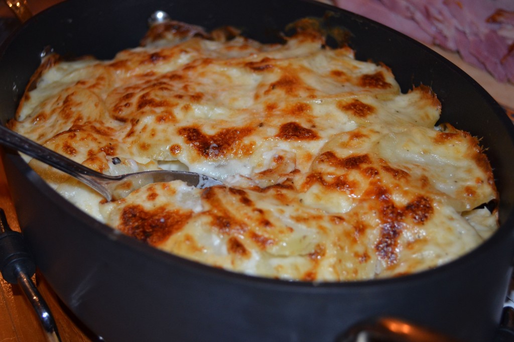 nicely browned scalloped potatoes in hard anodized oval pan with spoon