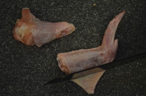 A knife is cutting away the flap of skin between the drumstick and the "flat" or middle segment of the chicken wing