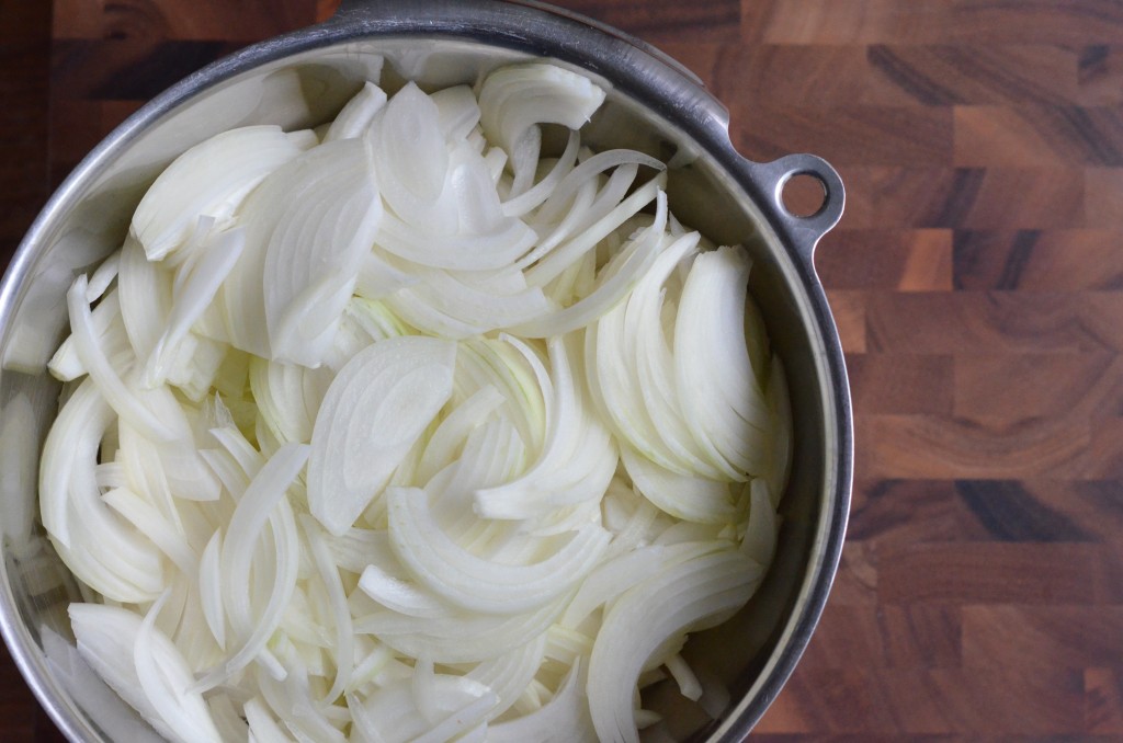 a stainless steel bowl full of sliced onions, resting on a wooden board