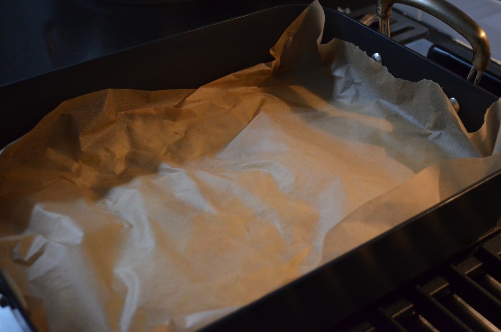 brown parchment paper pressed down on the onions in a hard anodized roasting pan