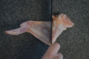 a hand holding a knife is cutting the drumette off the chicken wing