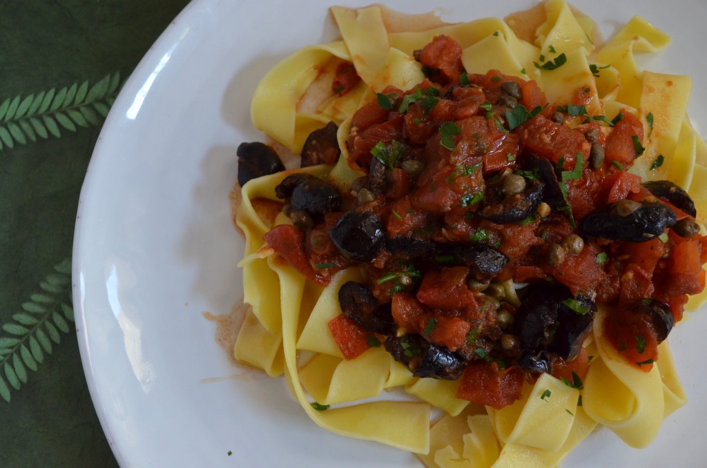 Papparelle with Putanesca sauce on top on a white plate on a green placemat