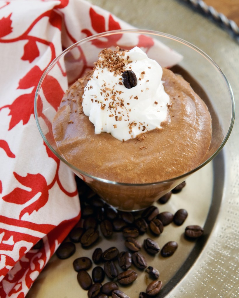 a martini glass with chocolate mousse, whipped cream and espresso bean on a metal tray with a red and white napkin
