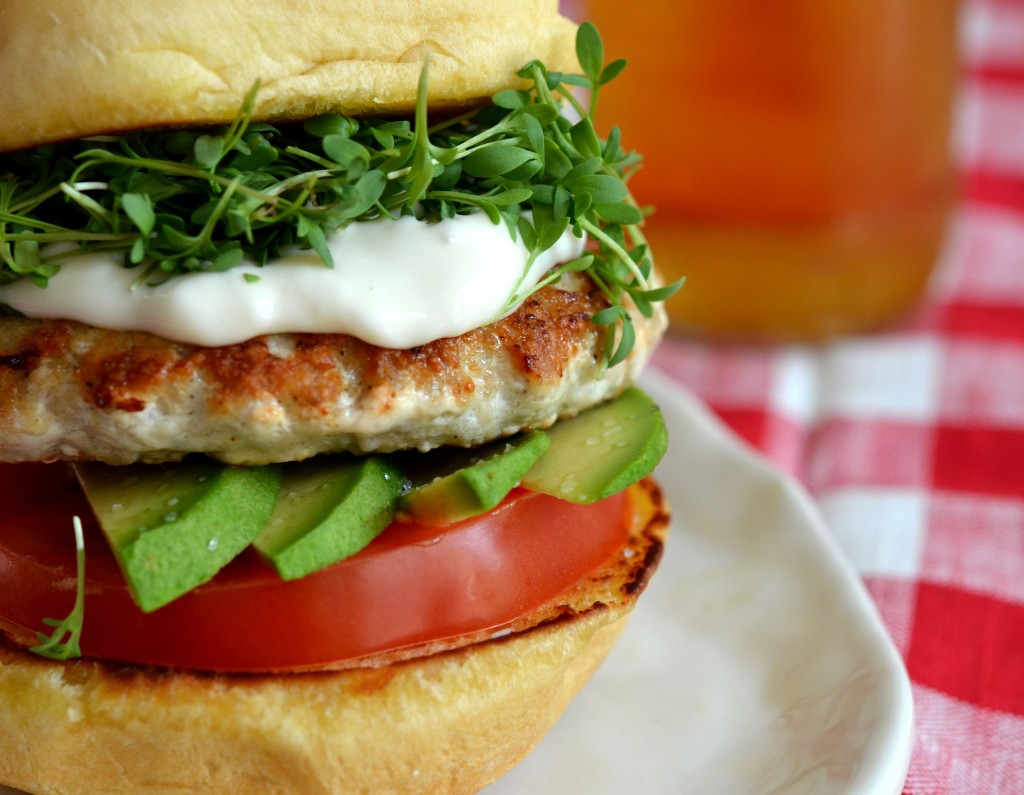 close up shot of a burger on a bun with tomato, avocado, mayonnaise and sprouts
