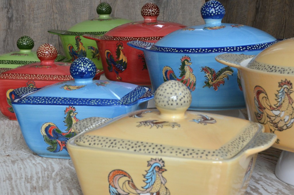 A row of all the different colored ceramic casseroles with the rooster design - tan, blue, red and green