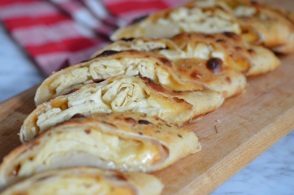 chicken cheesesteak stromboli sliced and fanned out on a wooden cutting board; red checkered napkin in background