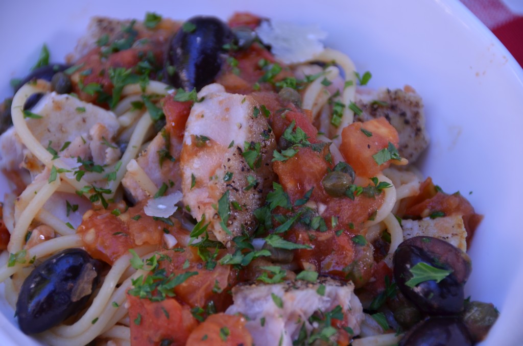 Spaghetti with tuna, tomatoes, capers, basil, olives in a white bowl