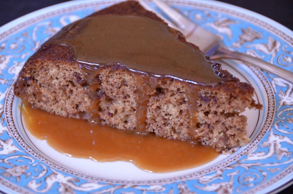 a wedge of sticky toffee pudding on a china plate with sauce dripping down the sides