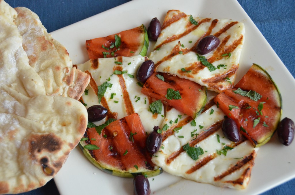 grilled halloumi and watermelon on  a white plate with griddle bread off to the side. Blue tablecloth background