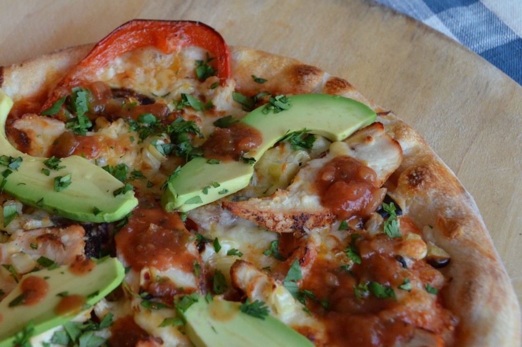 close up shot of the pizza with avocado, chicken and red pepper visible